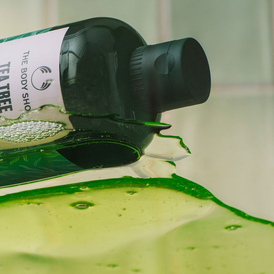 Imagen de un gel de ducha enriquecido con aceite de árbol de té, acompañado de hojas de árbol de té y elementos naturales que resaltan su fórmula natural y refrescante